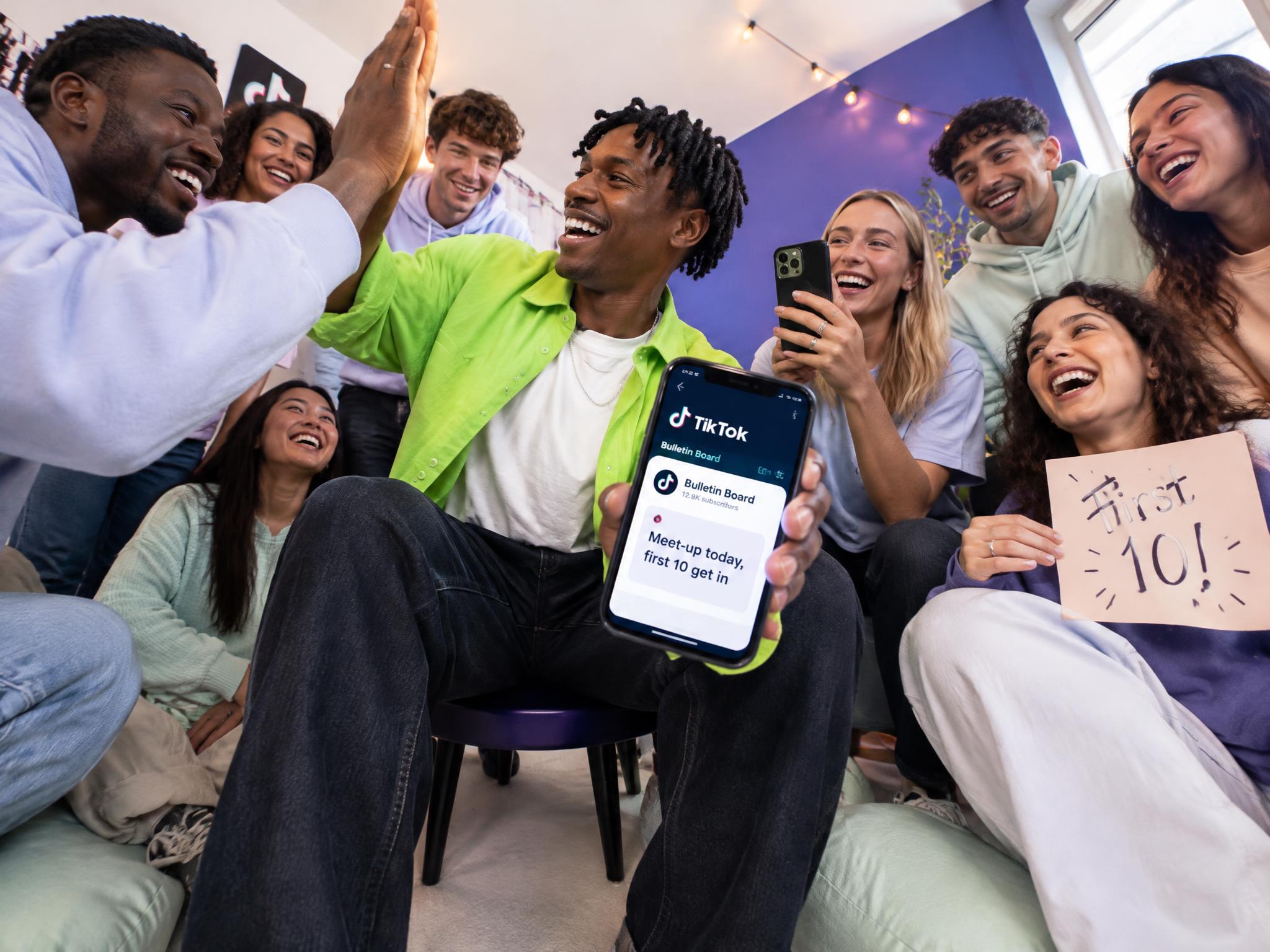 Creator showing a TikTok Bulletin Board message on his phone to a group of cheering followers