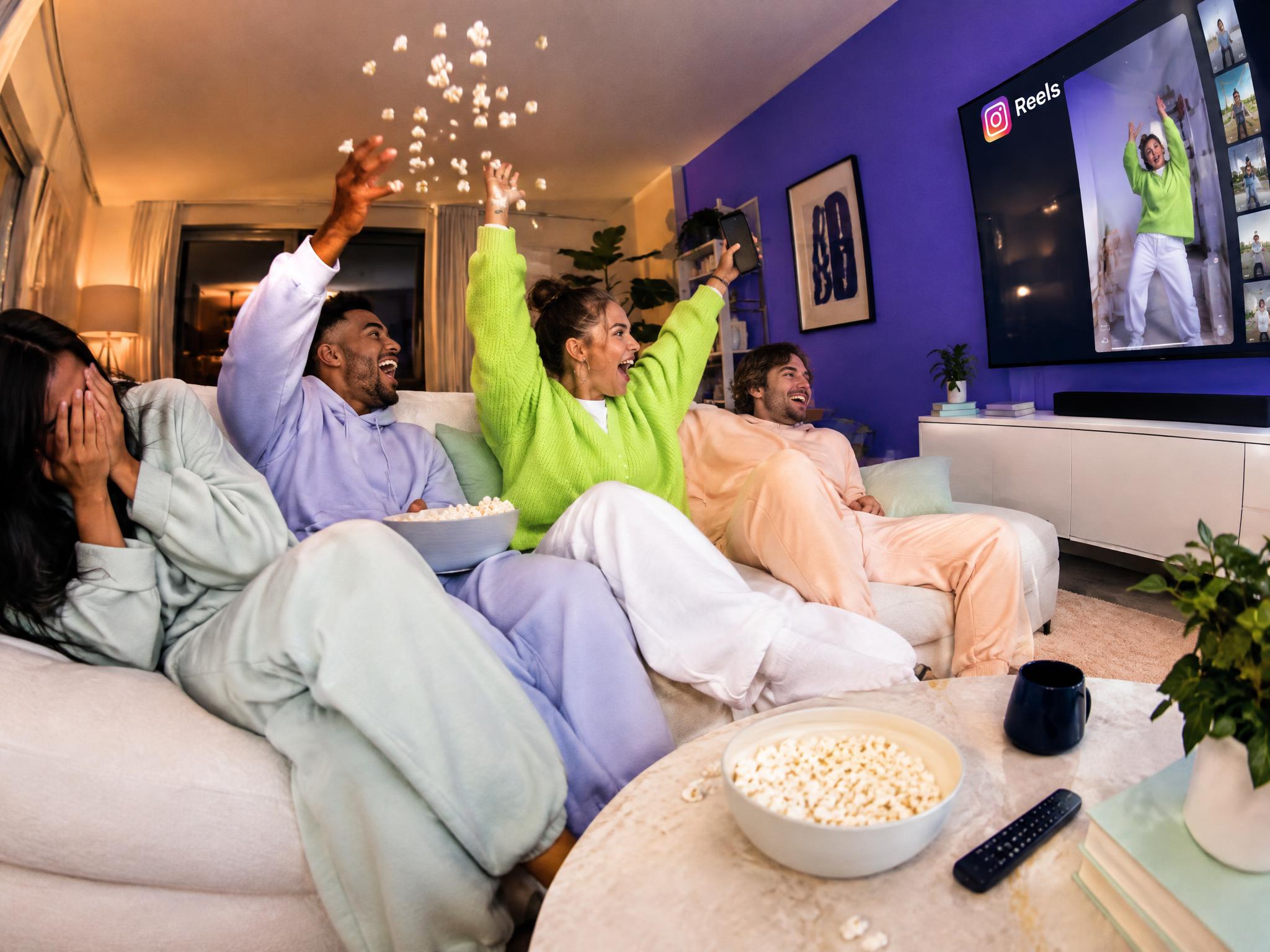 Friends on a sofa cheering while watching Instagram Reels on a TV