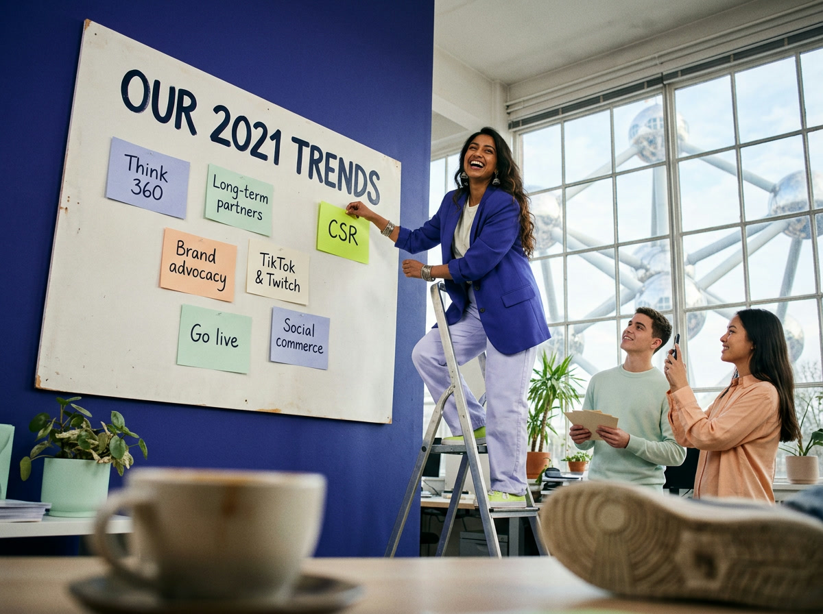 A woman on a stepladder adds a CSR note to a board titled "Our 2021 trends" while colleagues film her, with the Atomium outside the window