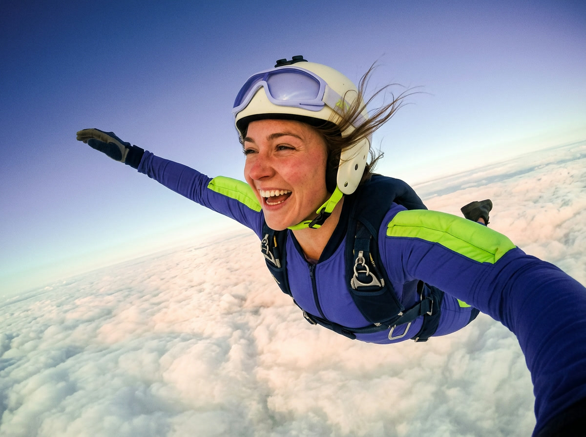 Smiling skydiver in a purple and lime suit in free fall above a sea of clouds